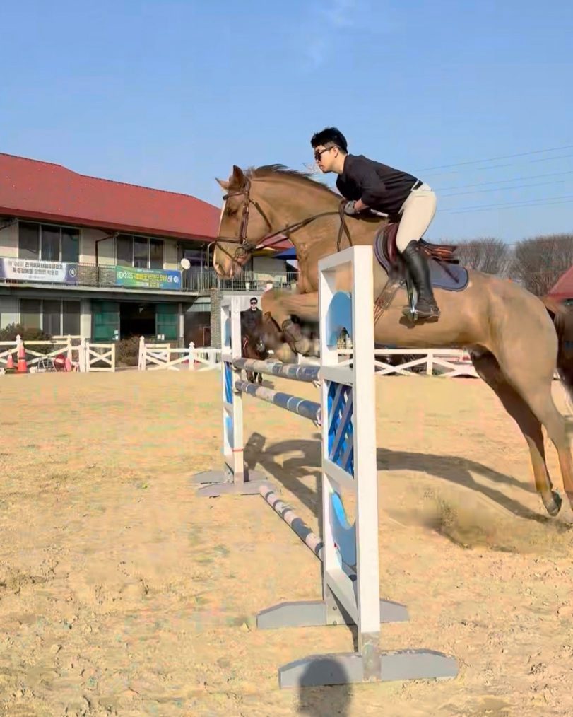Coach Kim Jinwoo jumping a fence in the arena in front of the clubhouse